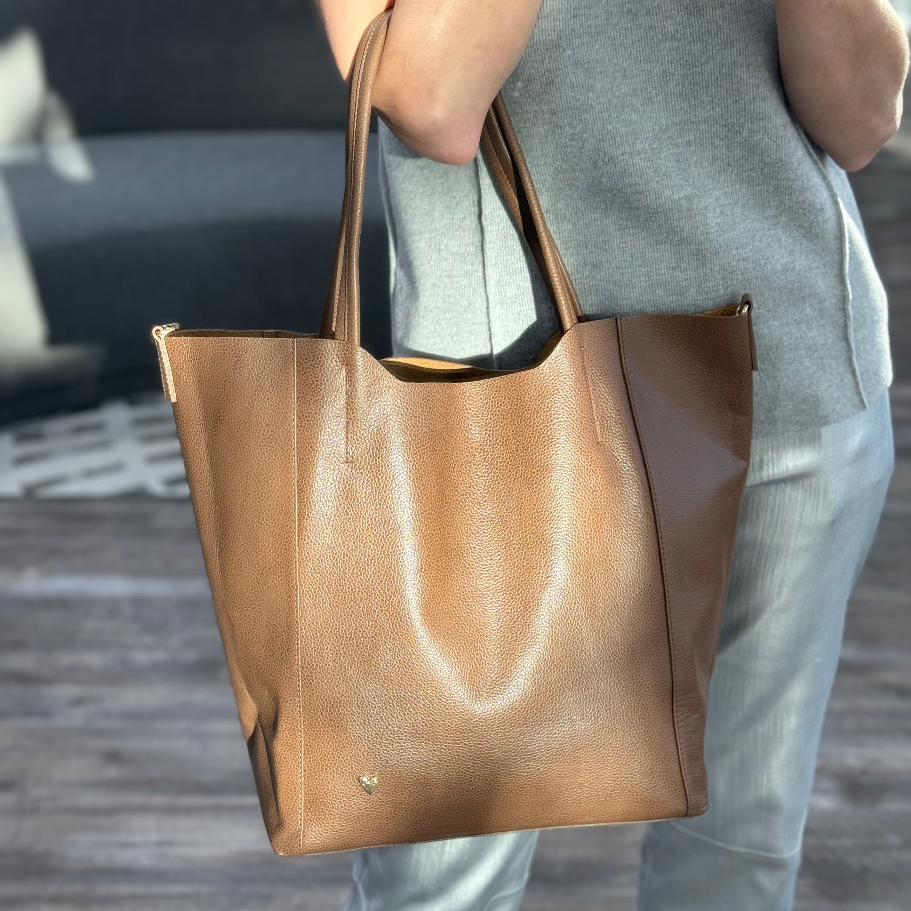 Parker Tote Leather Bag - Brown by Nataly Mendez, Genuine leather 21" H, 6.5" D Top: 9.5" W, Bottom: 13" W Handle Drop: 8.5"; Hook closure Flat zipped inside pocket Gold-color hardware Gold heart