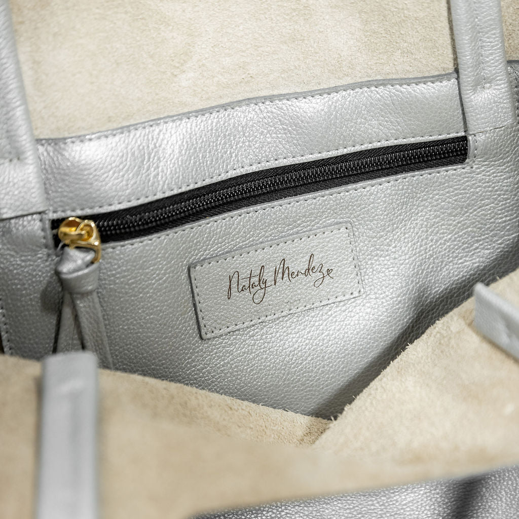 Parker Tote Leather Bag - Silver by Nataly Mendez, Genuine leather 21" H, 6.5" D Top: 9.5" W, Bottom: 13" W Handle Drop: 8.5", Hook closure Flat zipped inside pocket Gold-color hardware Gold heart